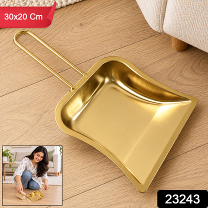 A gold-tone metal dustpan with a loop handle is on a wooden floor, with a small inset showing a woman using it.