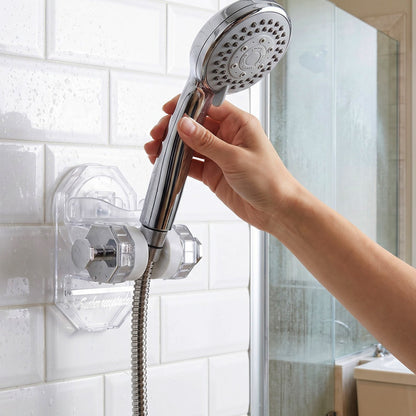 A hand holds a chrome shower head attached to a clear plastic wall mount.