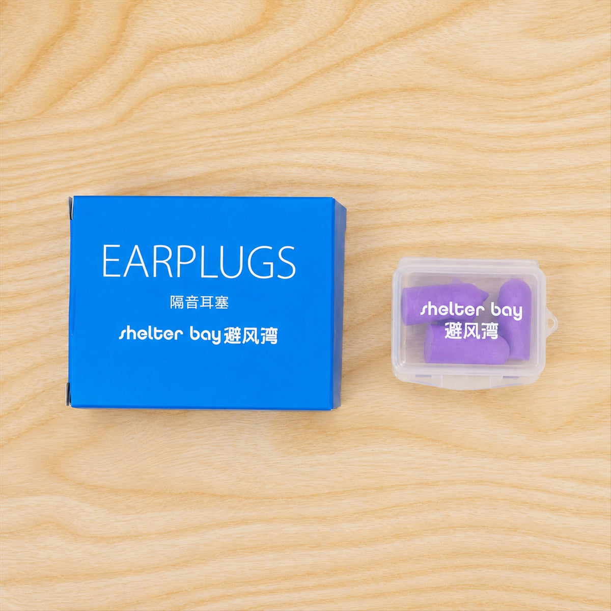 A blue box and a clear plastic case containing purple earplugs, both resting on a light wooden surface.