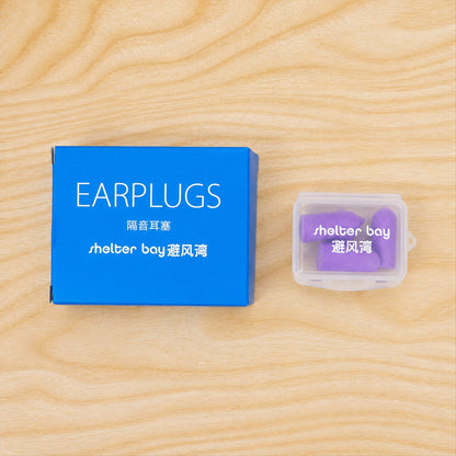 A blue box and a clear plastic case containing purple earplugs, both resting on a light wooden surface.