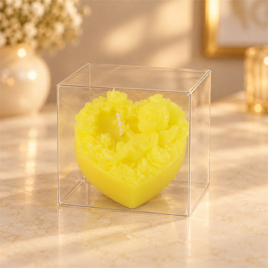 A vibrant yellow heart-shaped candle with intricate floral and cherub details, encased in a clear plastic box.