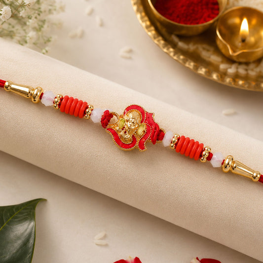 A red and gold Ganesha charm is centered on a red thread, flanked by red ribbed beads and white translucent beads.