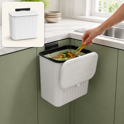 A person drops food scraps into a white ribbed compost bin with an open lid, mounted on a green kitchen cabinet.