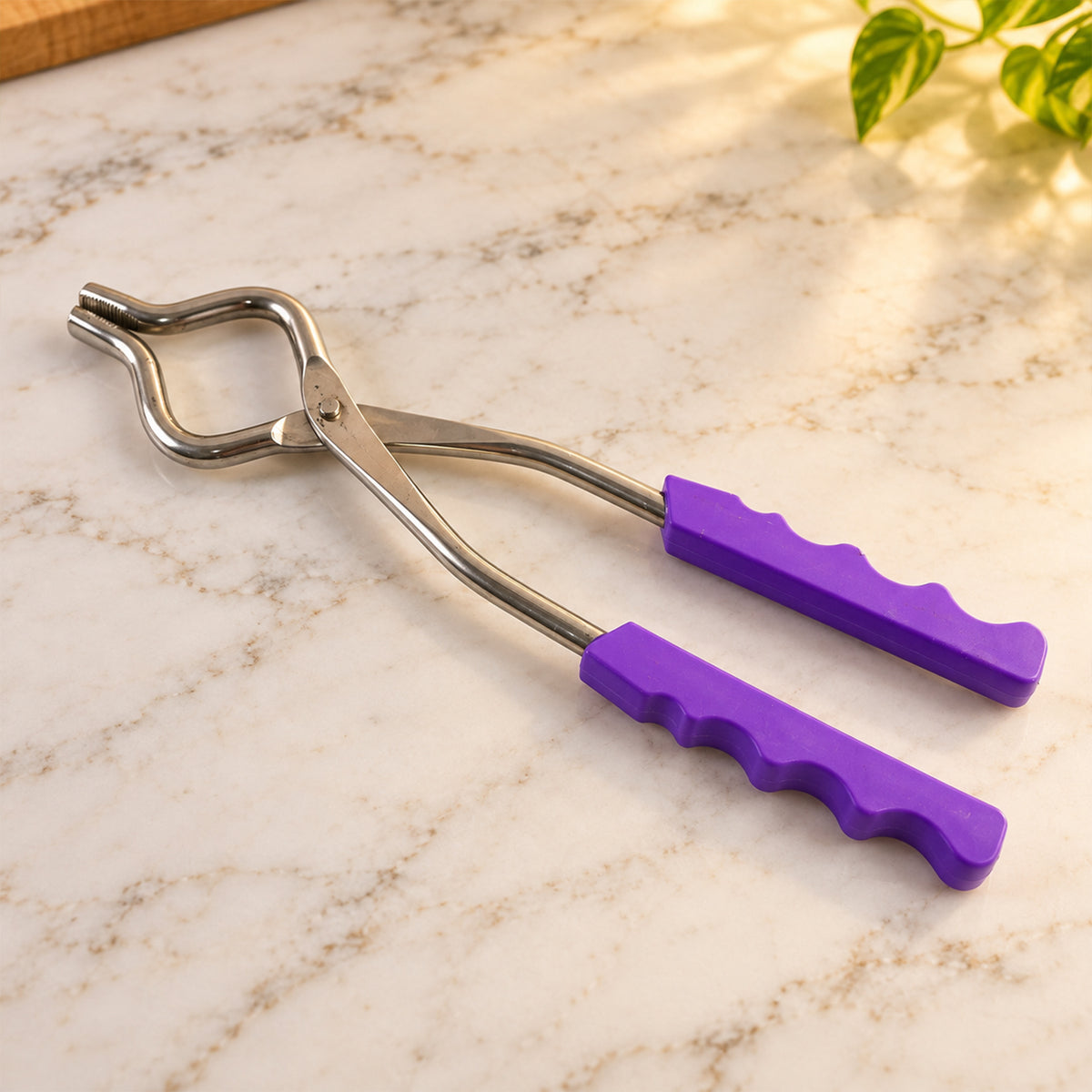 A stainless steel pot lifter with purple handles resting on a white marble countertop with soft lighting.