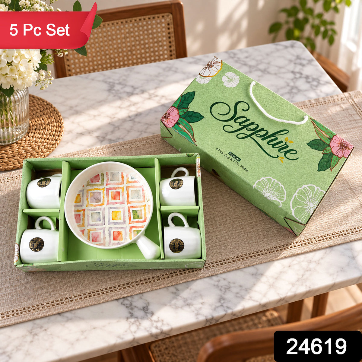 A green gift box holds a five-piece ceramic set, with four white mugs and a platter featuring a vibrant geometric design.