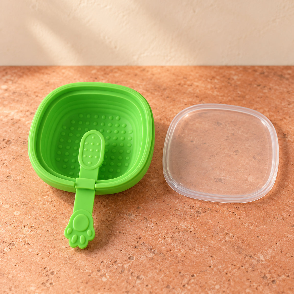 A vibrant green silicone ice cream mold with a paw-shaped handle and a clear lid sits on a brown textured surface.