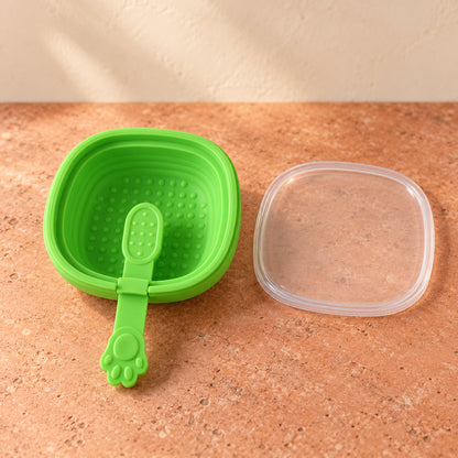 A vibrant green silicone ice cream mold with a paw-shaped handle and a clear lid sits on a brown textured surface.