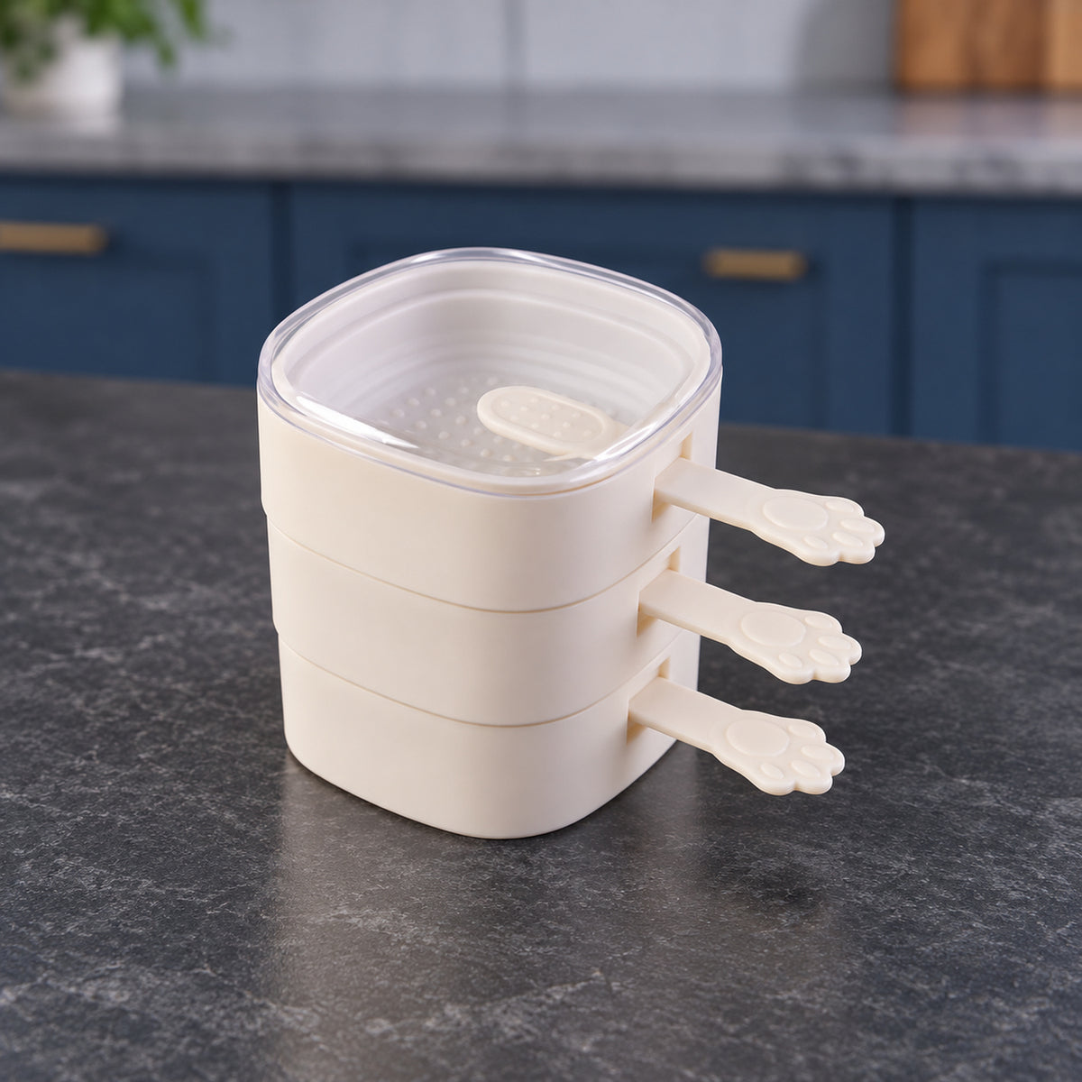 A stack of three beige square molds with paw handles and a clear lid, sitting on a dark countertop.