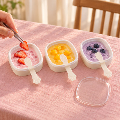 Three square molds with paw handles, filled with colorful purees, being topped with fresh strawberry slices by tweezers.
