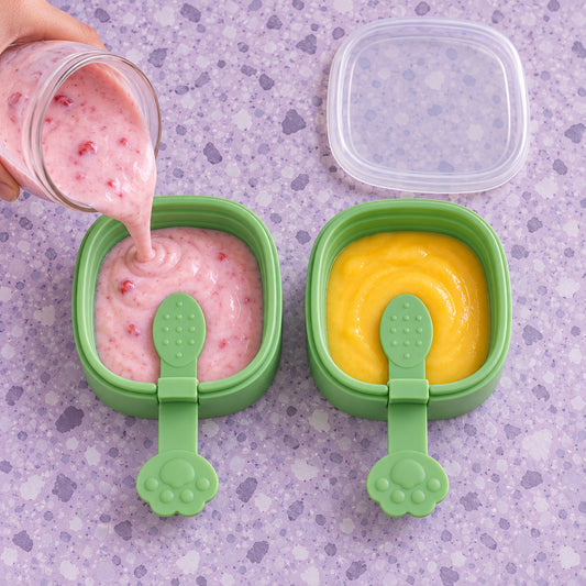 A hand pours pink liquid into a green square mold with a paw-shaped handle, beside another mold filled with yellow liquid.