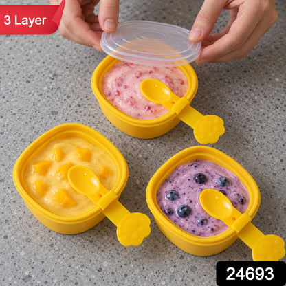 Three yellow square molds filled with different fruit purees, each with a paw-shaped spoon, one lid being placed. – view 9