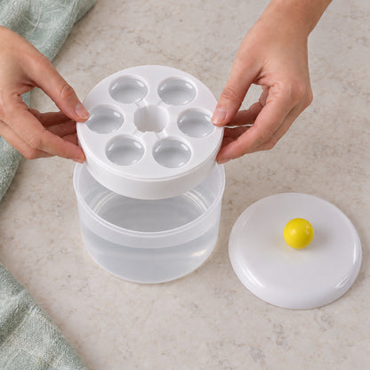 Two hands remove the white ice cube tray with six circular molds from the translucent container, revealing water below.
