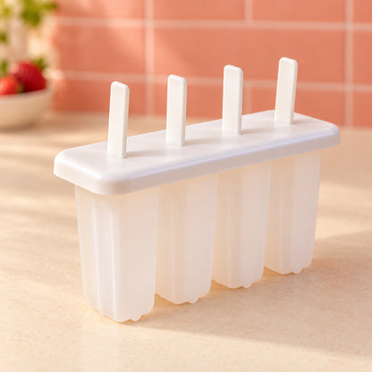 A white 4-cavity popsicle mold with sticks stands on a light countertop, with a blurred background of a kitchen setting.