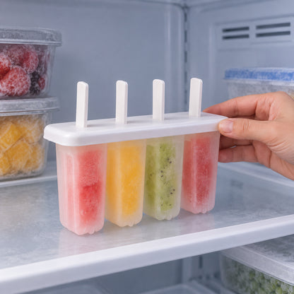 A hand places a white 4-cavity popsicle mold filled with colorful frozen treats onto a shelf inside a refrigerator.