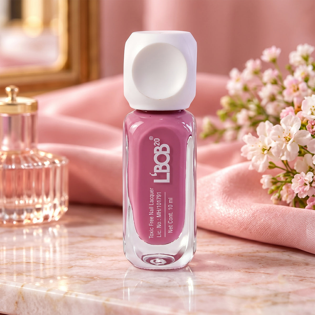 A small glass bottle of mauve nail polish with a white square cap sits on a pink marble surface.