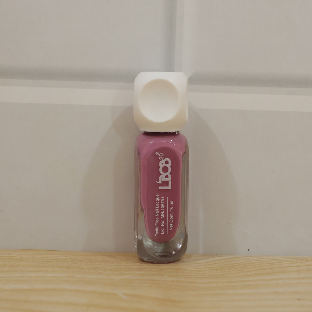 Hand holding mauve rose colour nail polish bottle during manicure