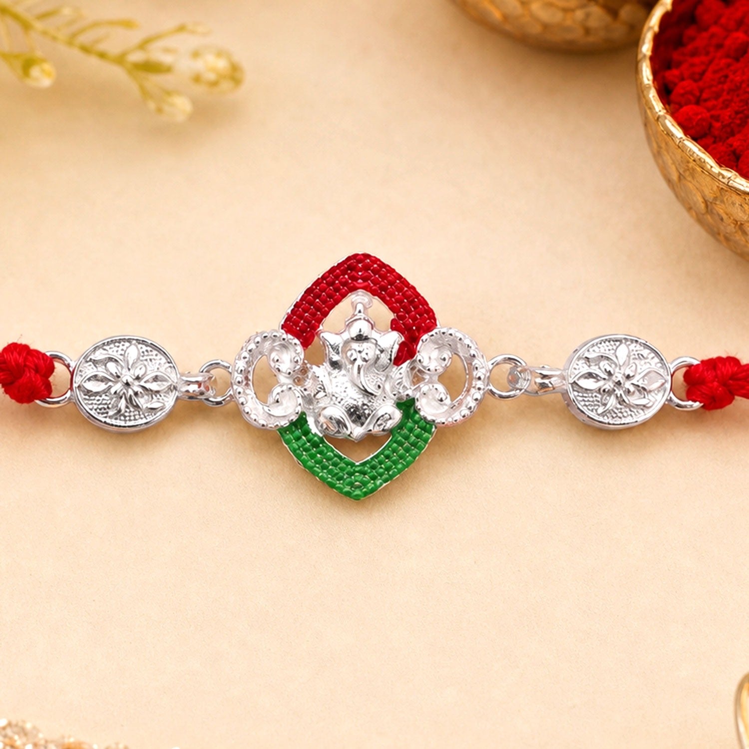 Silver Green Floral Rakhi with red thread and side charms on a white background