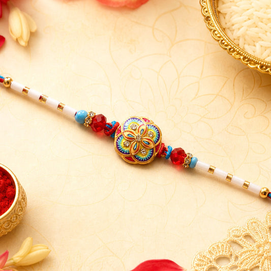 A vibrant floral bead bracelet with red, blue, and yellow enamel sits on a patterned cream surface with flower petals and