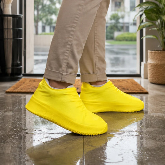 A person wearing khaki pants and bright yellow silicone shoe covers stands on a wet tiled floor near a doorway.