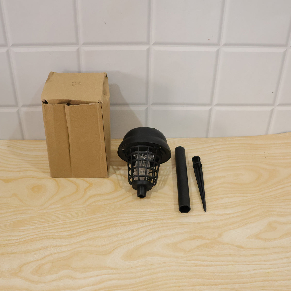 A cardboard box and the three components of the black solar lamp are arranged on a light wooden surface.