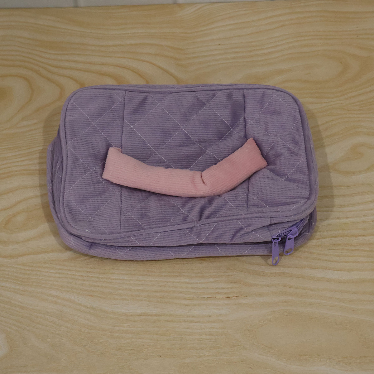 A closed lavender quilted corduroy cosmetic bag with a pink handle and a pink and green tulip applique, shown from a