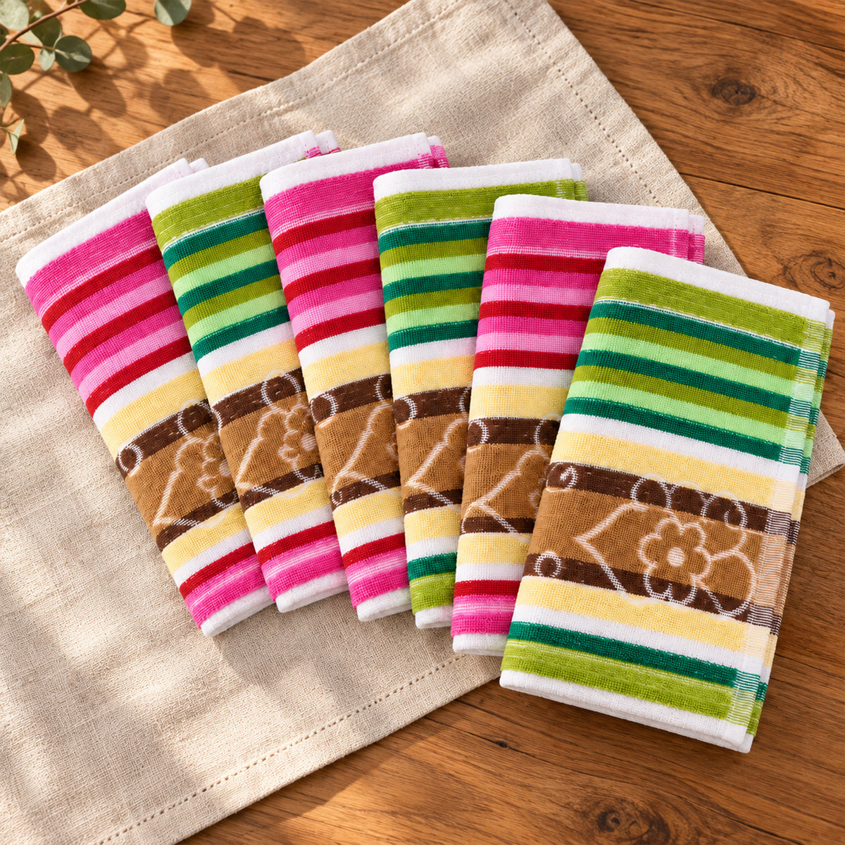 Six folded cloths with pink, white, green, and brown stripes and a floral pattern are arranged on a light brown linen fabric.