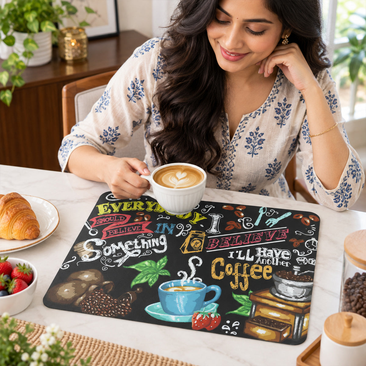 A woman smiles while holding a white coffee cup, with the coffee-themed mat on a light-colored table beside her.