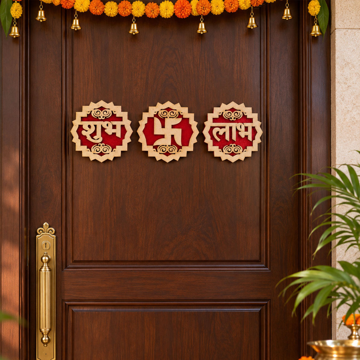 Three wooden and red velvet Shubh Labh Swastik decorations adorn a dark brown door, with marigold garlands overhead.