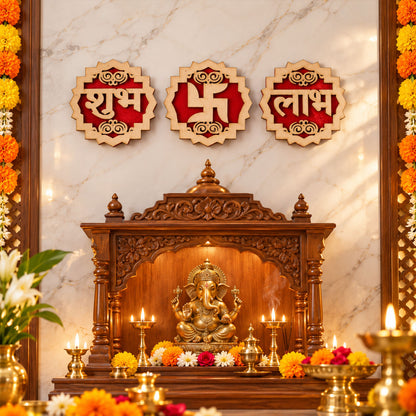 Three decorative wooden and red velvet Shubh Labh Swastik pieces hang above a carved wooden altar with a golden Ganesha idol.
