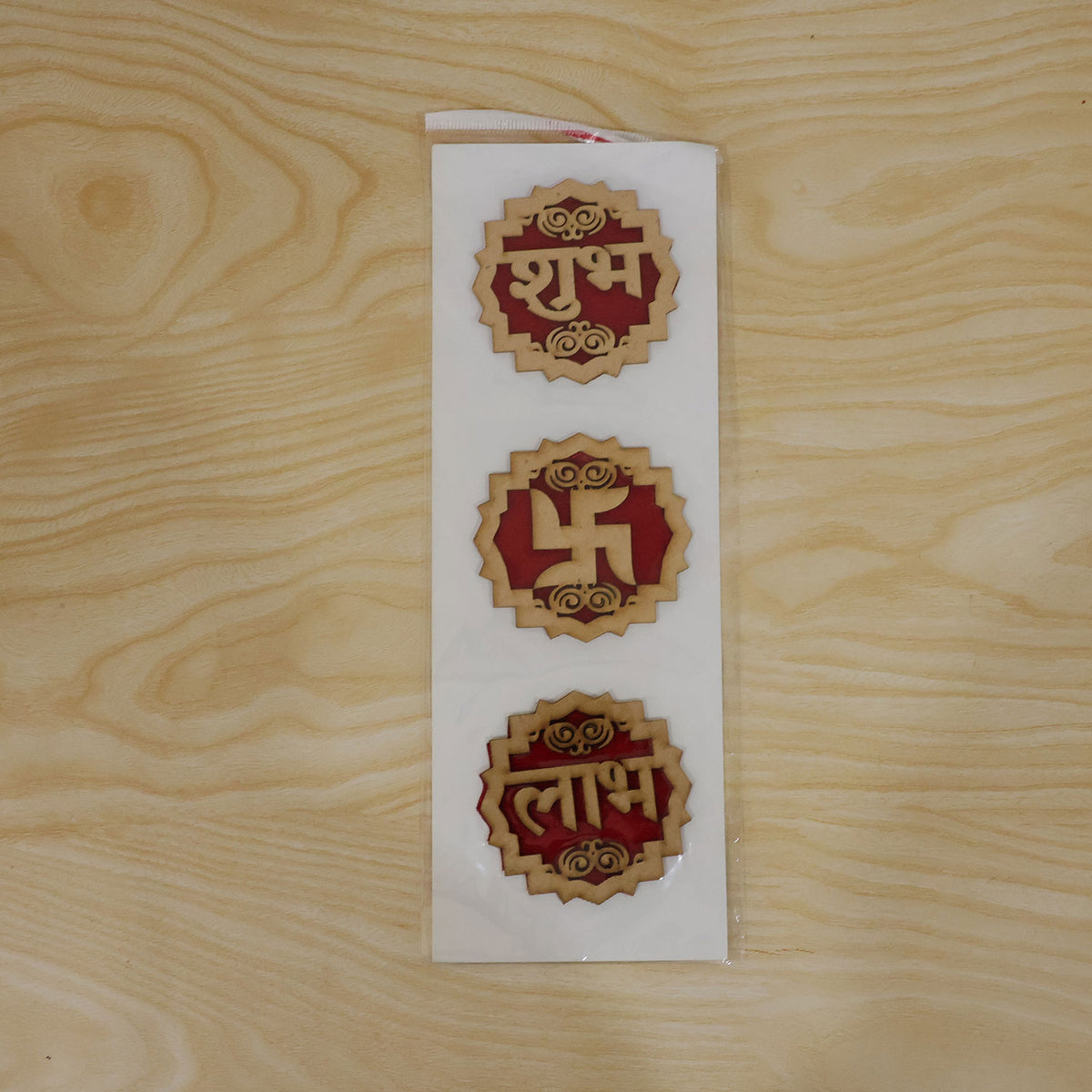 The three wooden Shubh Labh Swastik decorations are shown in clear plastic packaging on a light wooden surface.