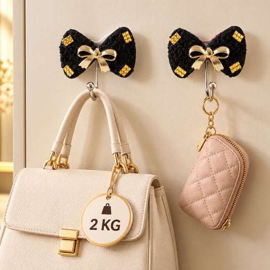 Two black bow-shaped hooks with gold accents and a gold bow, holding a white handbag and a pink quilted pouch.