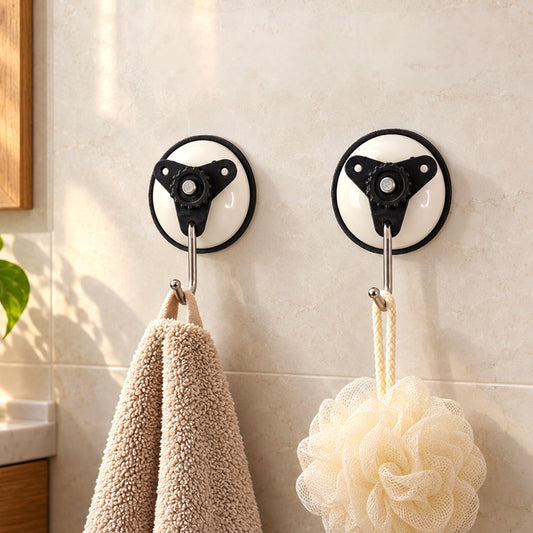 Two white and black suction cup hooks with metal hangers on a tiled wall, holding a beige towel and a cream bath pouf.