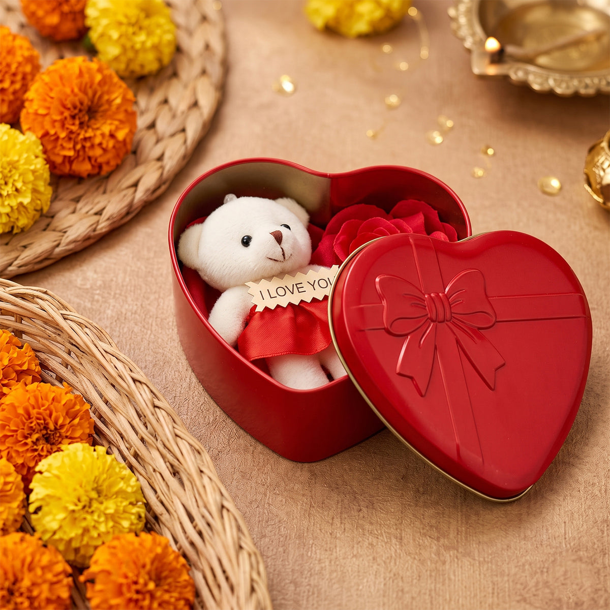 A red heart-shaped box contains a small white teddy bear and a red artificial rose, beside a woven basket.