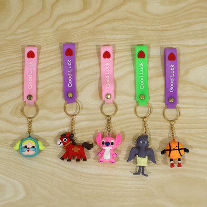 Five unique cartoon character keychains with colorful silicone straps and gold rings are laid out on a light brown wooden