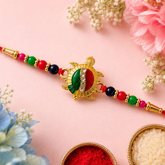 A gold turtle charm with green, red, and white enamel, plus clear stones, is centered on a red thread with colorful beads.