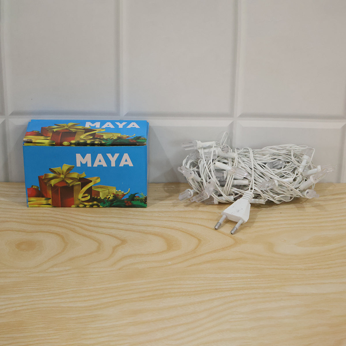 A blue Maya brand box and a coiled white string of LED lights with a plug on a light wooden surface.