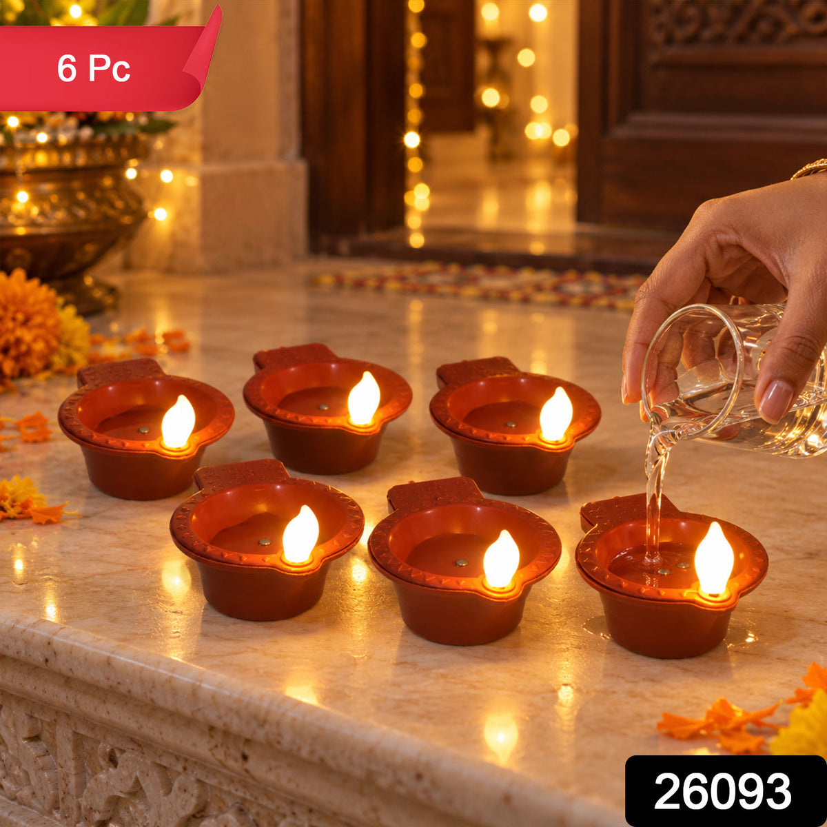 A hand pours water into one of six glowing terracotta-colored LED diyas, arranged on a textured surface with festive lights.