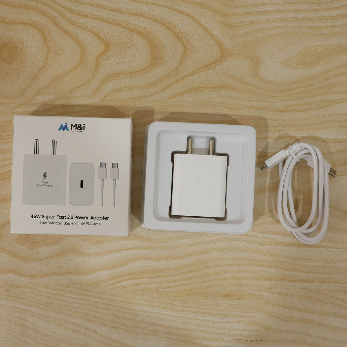 The white charger, its box, and a coiled white USB-C cable on a light wooden background.