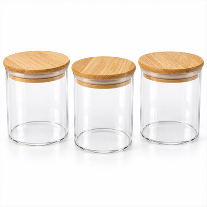 Three empty clear glass jars with light brown bamboo lids arranged in a row on a white surface.