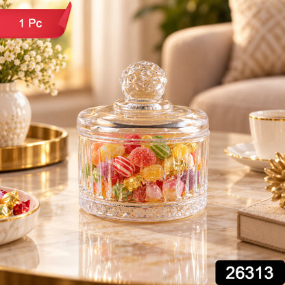 Glass candy bowl with lid, full of various candies, on a table next to a white vase and gold tray.