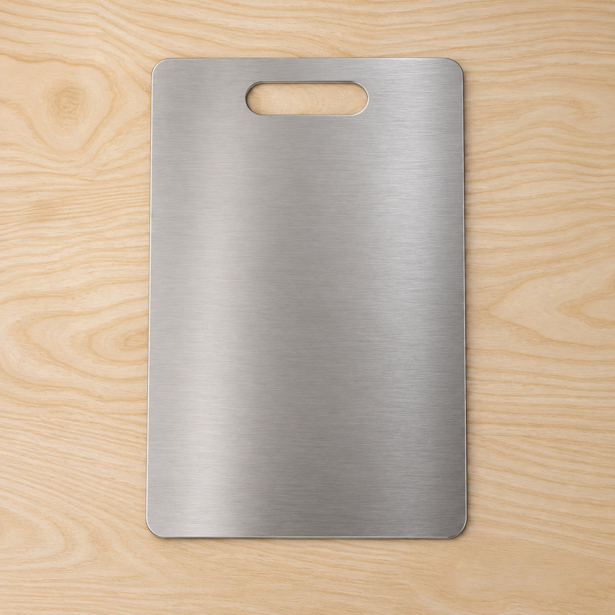 A rectangular brushed stainless steel cutting board with an integrated handle, positioned centrally on a light wooden