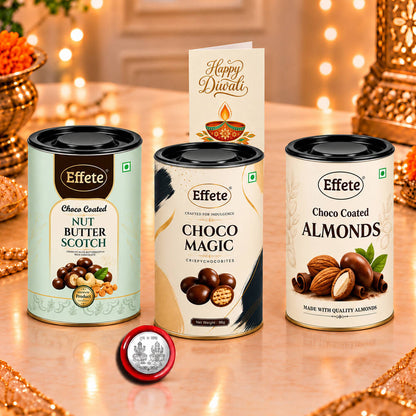 Three tins of chocolate-covered nuts and a Diwali greeting card on a table with warm, blurred lights.