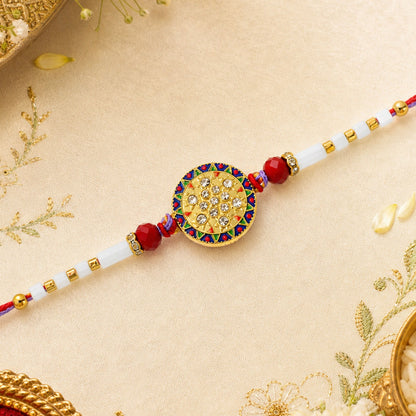 A gold, red, and white beaded bracelet with a round, ornate centerpiece featuring clear stones, on a light gold fabric.