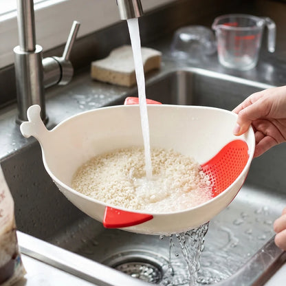 A person rinsing rice in a white whale-shaped bowl with red accents under a kitchen faucet, water draining into the sink.