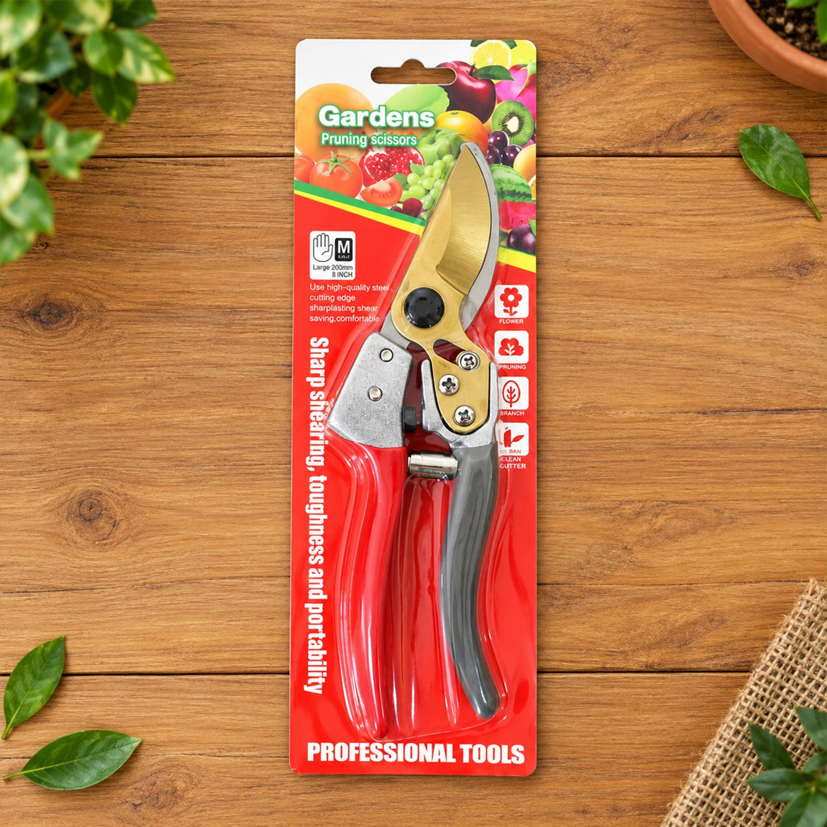 Red and grey pruning shears with golden blades in retail packaging on a wooden surface.