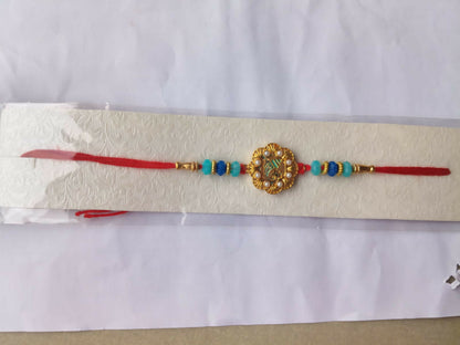 The Ganesha charm bracelet, with its red thread and blue beads, is displayed on a textured white paper card.