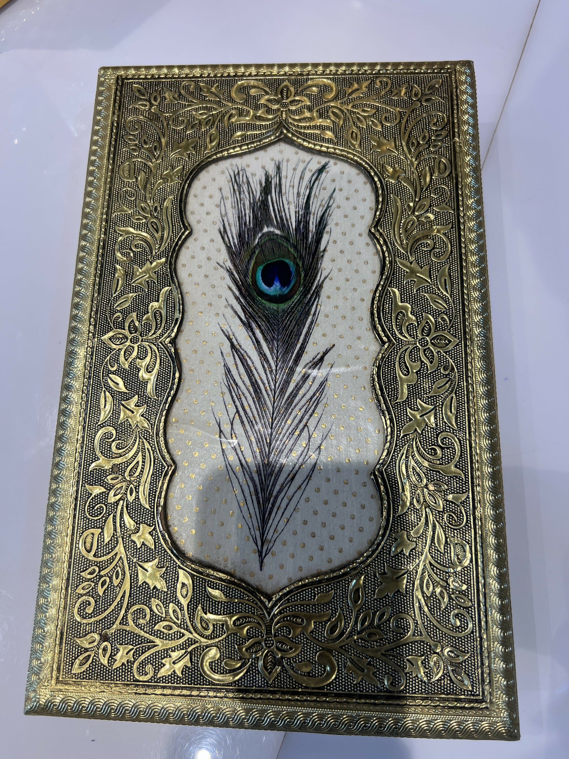 Stylish compact gold jewelry box with embossed peacock feather design on dresser