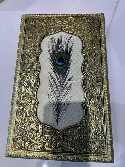 Stylish compact gold jewelry box with embossed peacock feather design on dresser