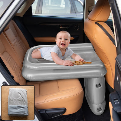 A smiling baby lies on a gray inflatable bed, which is placed across the back seats of a car with tan leather upholstery.