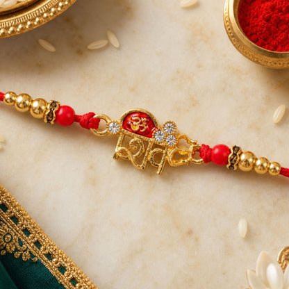 A red thread bracelet with golden beads and a central gold-toned charm featuring a red Om symbol and clear stones.